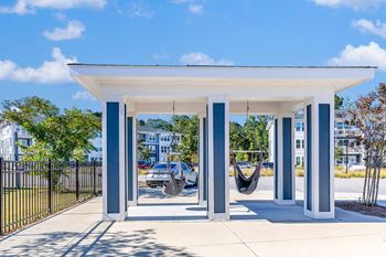 A white and blue structure with a hammock in front of a parking lot.